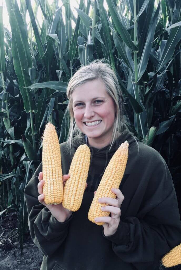 Hannah Taylor holding 3 corn stalks in front of farm